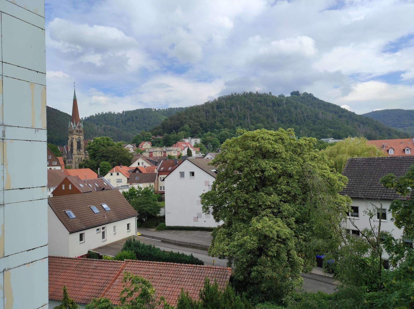 Panoramablick auf ein Dorf mit Kirche und bewaldeten Bergen im Hintergrund.