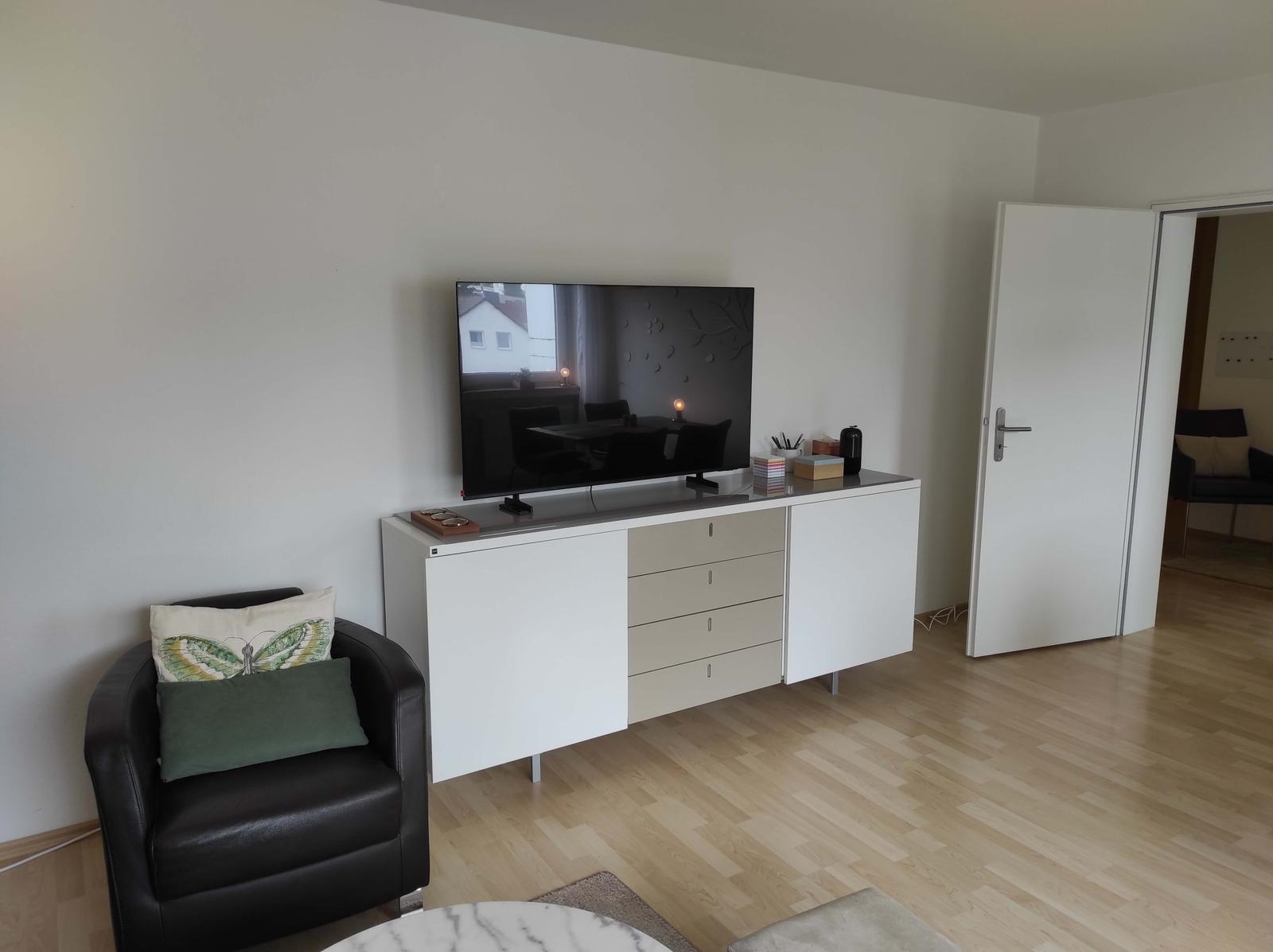 Ein Wohnzimmer mit Fernseher, Schrank und Sessel.