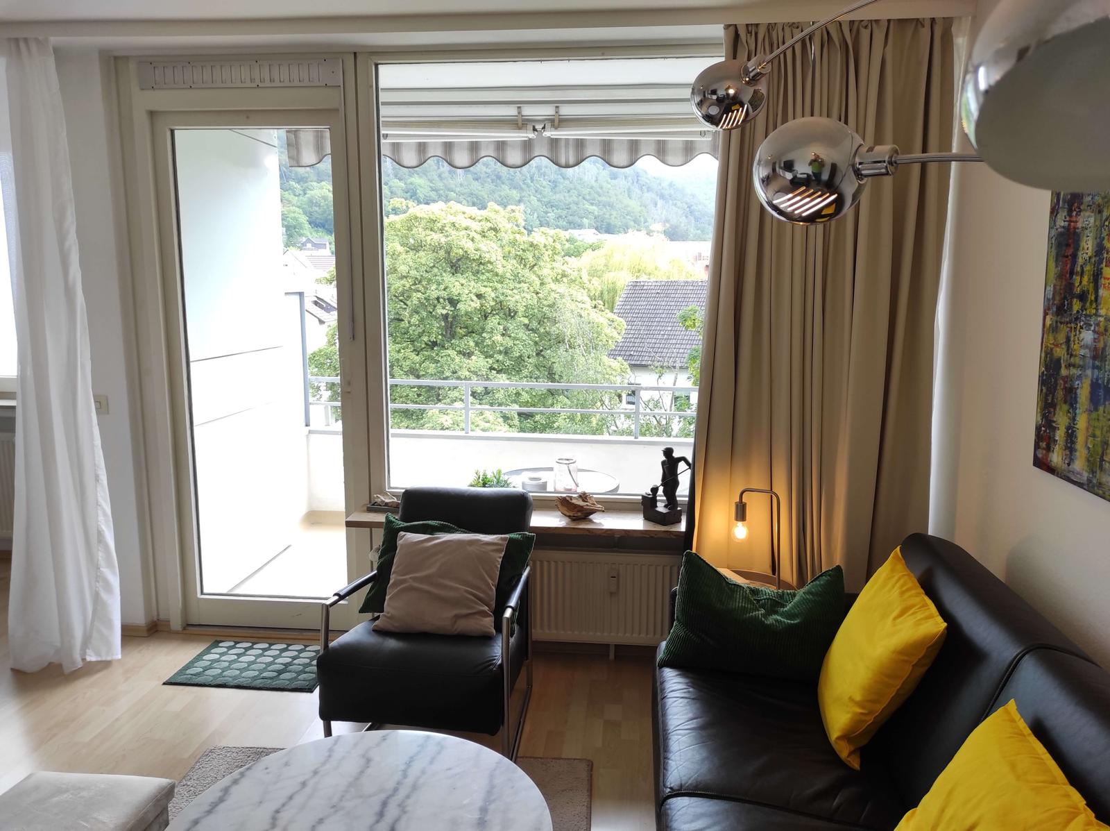 Wohnzimmer mit Blick auf grüne Landschaft. Sofa und Sessel mit Kissen.