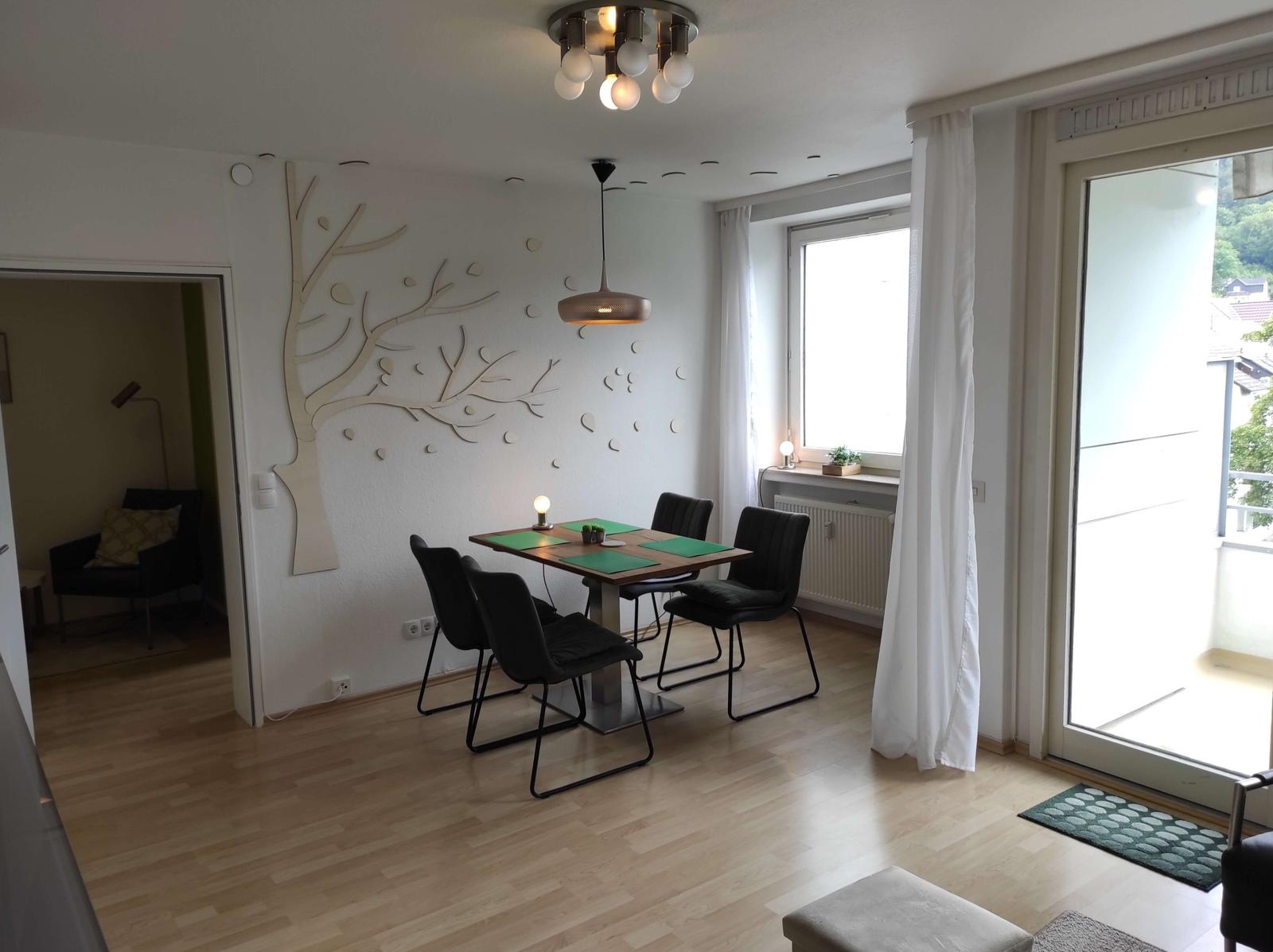 Essbereich mit Tisch, Stühlen und Wanddekoration. Durchgang zum Wohnzimmer. Terrasse über Glastür.