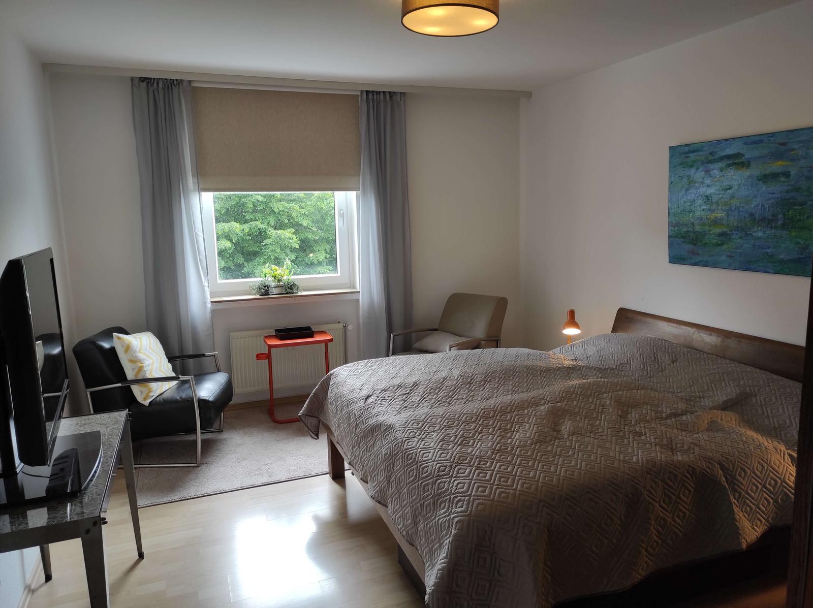 Schlafzimmer mit Bett, Sessel, Fenster und Wandbild.