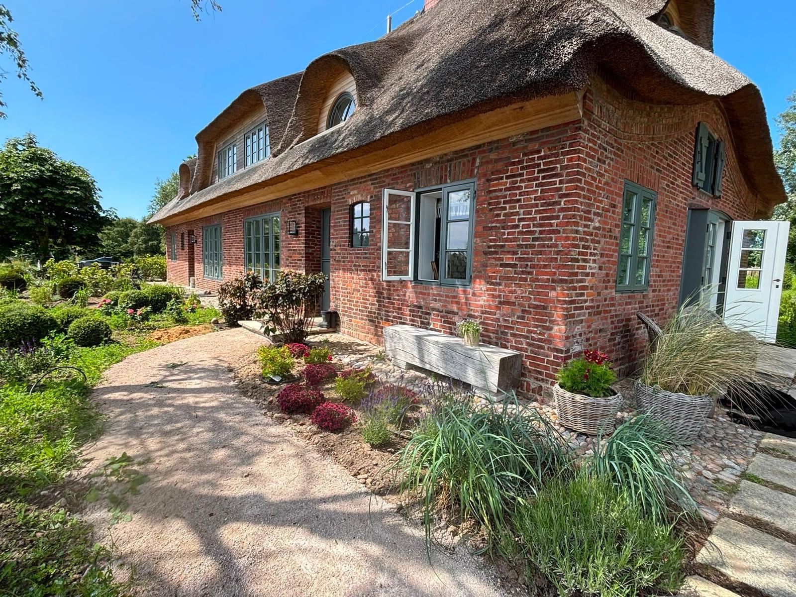 Rotes Backsteinhaus mit Strohdach und grünen Fenstern im Garten