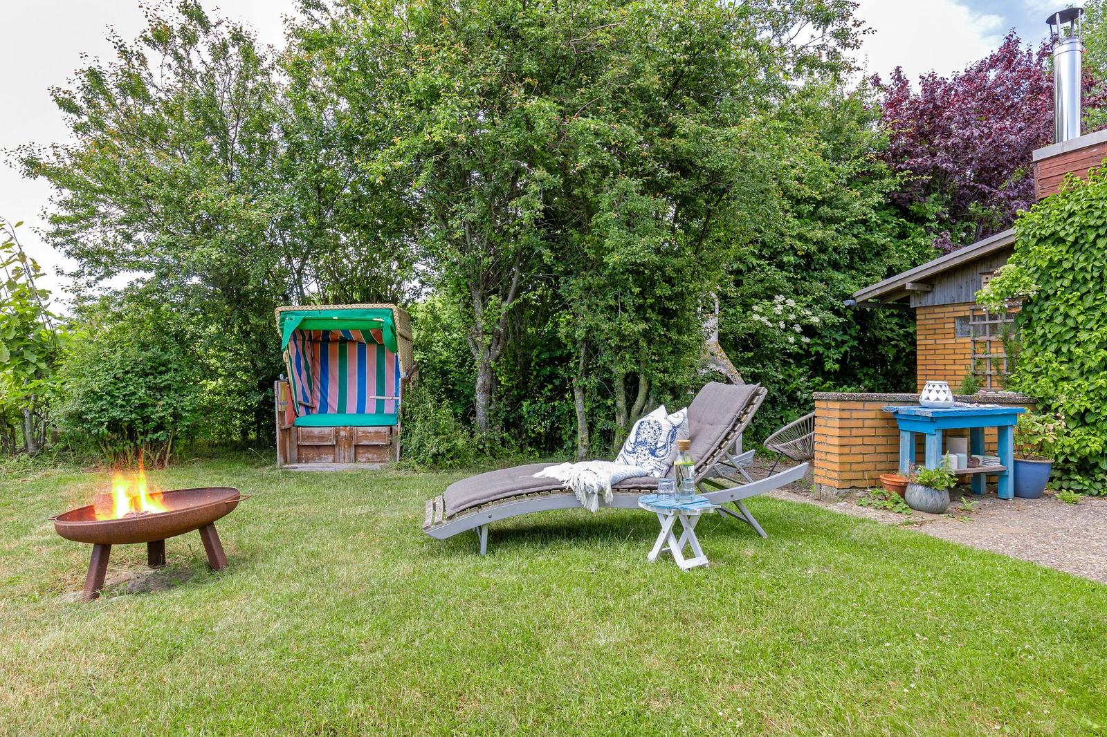 Hinterhof mit Liege, Feuerkorb und Strandkorb. Grünfläche und Baumreihe.