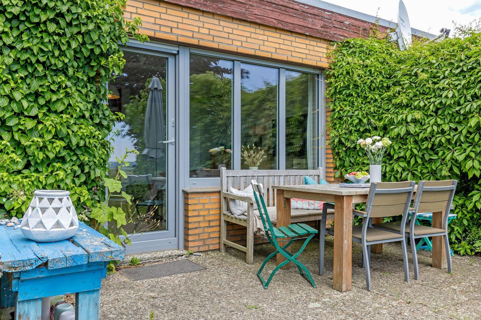Terrasse mit Tisch, Stühlen und grüner Wand. Durchgangstür führt ins Haus.