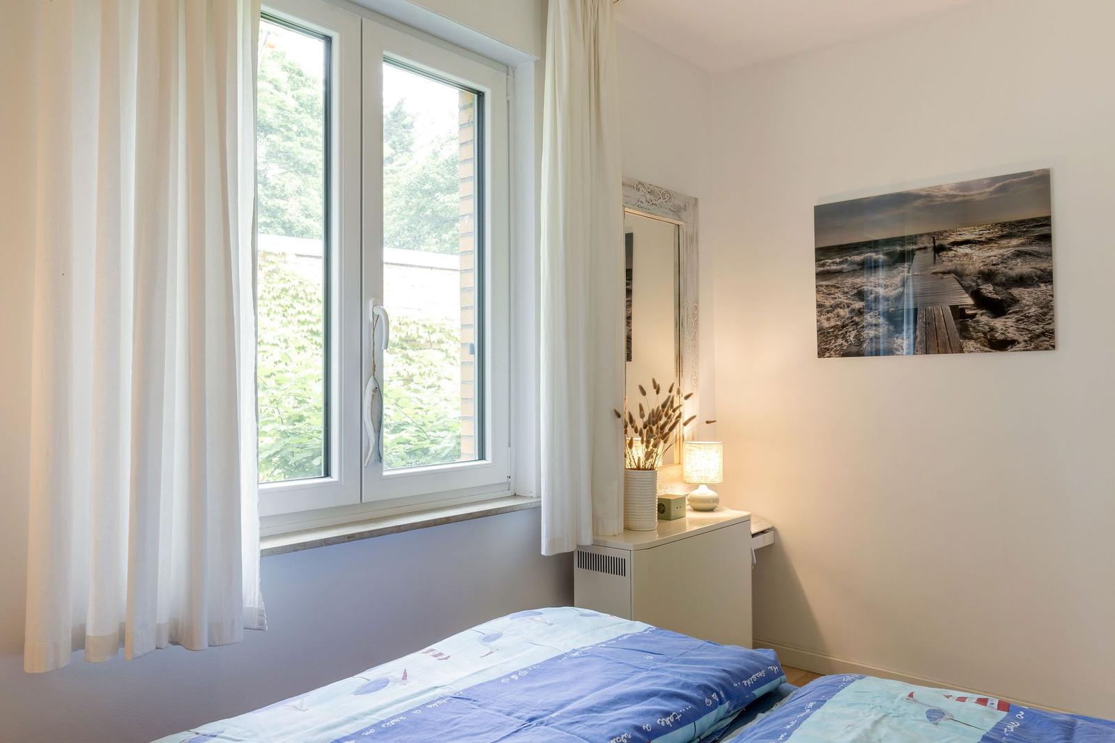 Schlafzimmer mit Fenster, Spiegel und Wandbild.