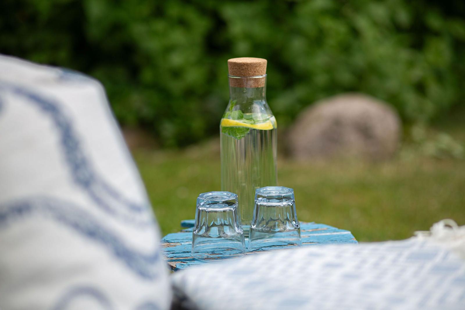 Auf einem blauen Tisch steht eine Glasflasche mit Wasser, Minze und Zitrone sowie zwei Gläser.