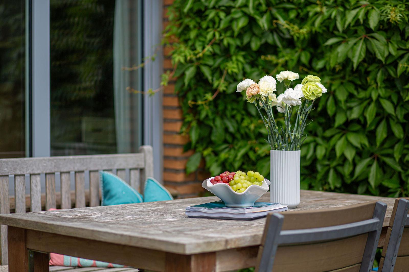 Holztisch mit Blumen, Trauben und Büchern im Garten