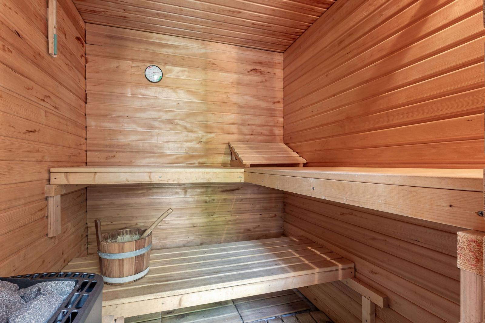 Sauna mit Holzbanken, Thermometer und Eimer mit Besen.