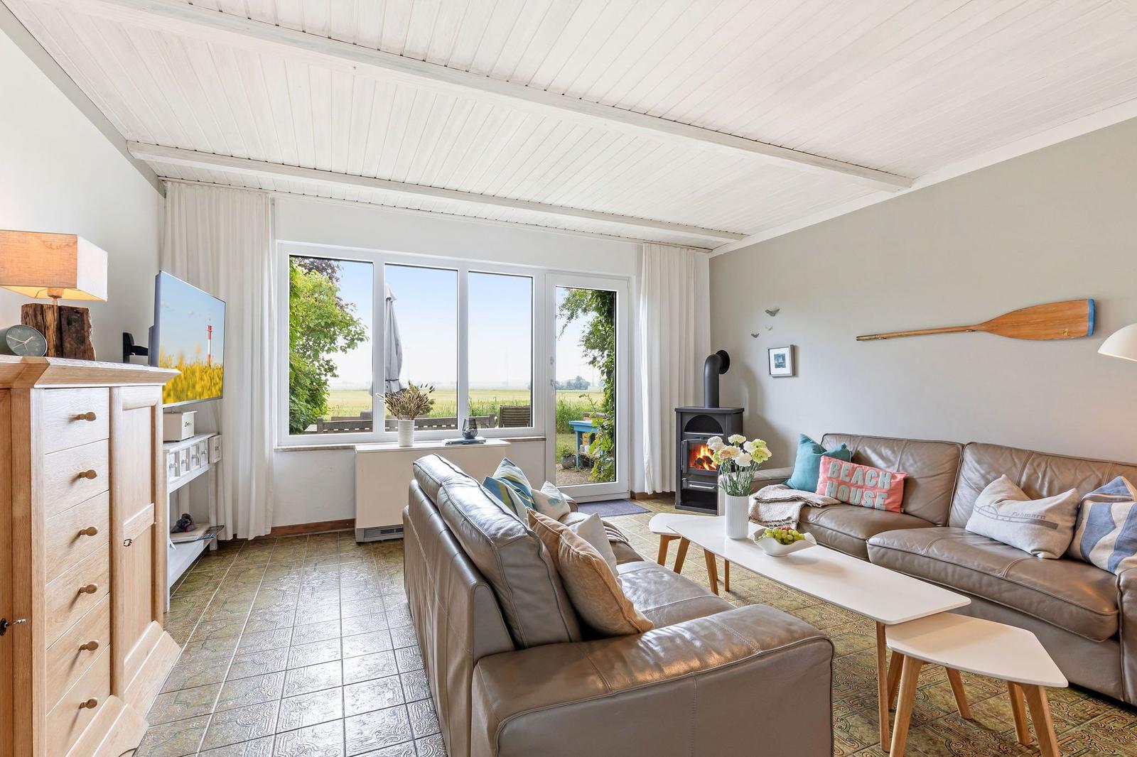 Wohnzimmer mit Ledersofa, Kamin und großem Fenster zum Garten.
