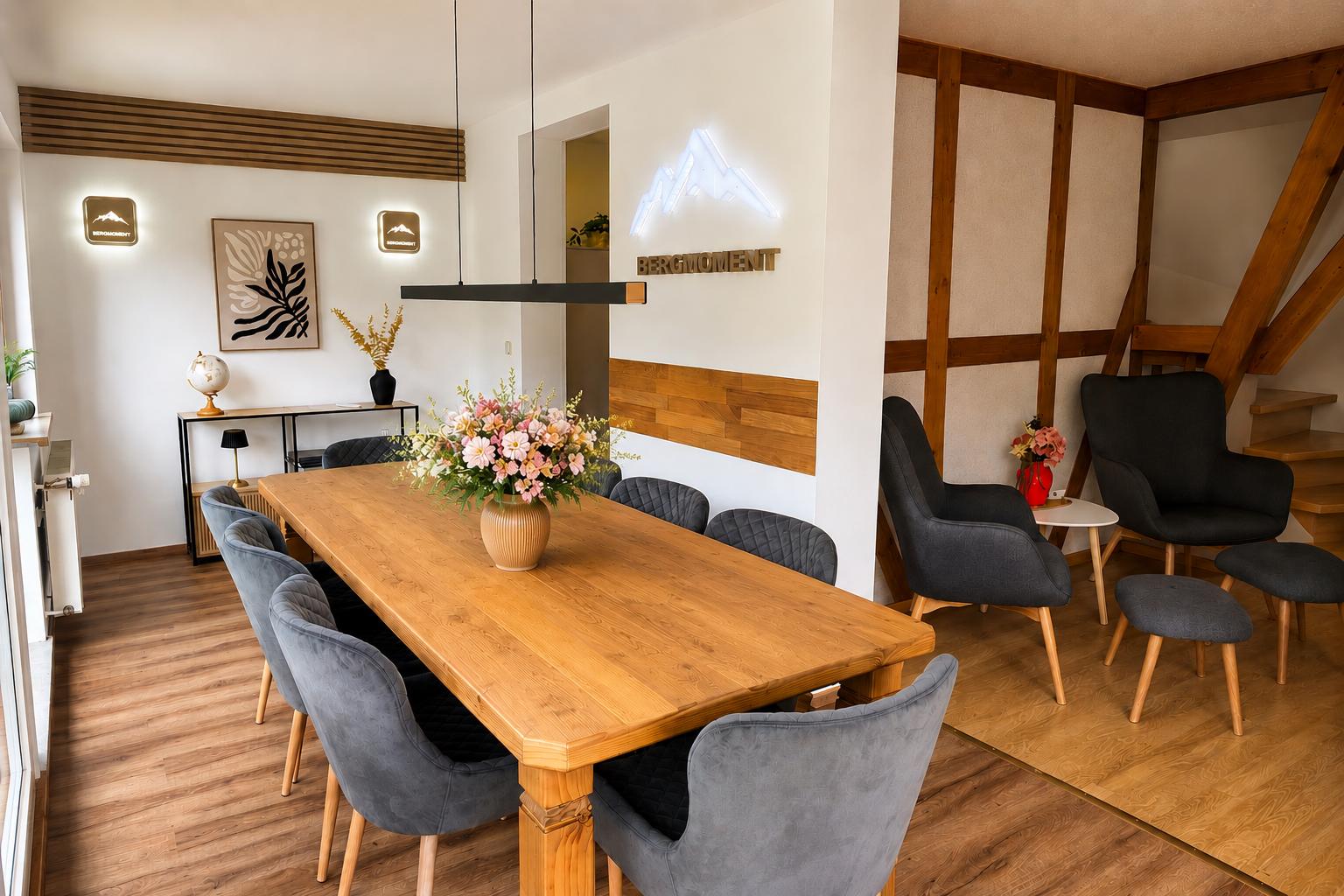 Esszimmer mit Holztisch, grauen Stühlen und Blumenarrangement. Wandgestaltung mit Holz und Neon.