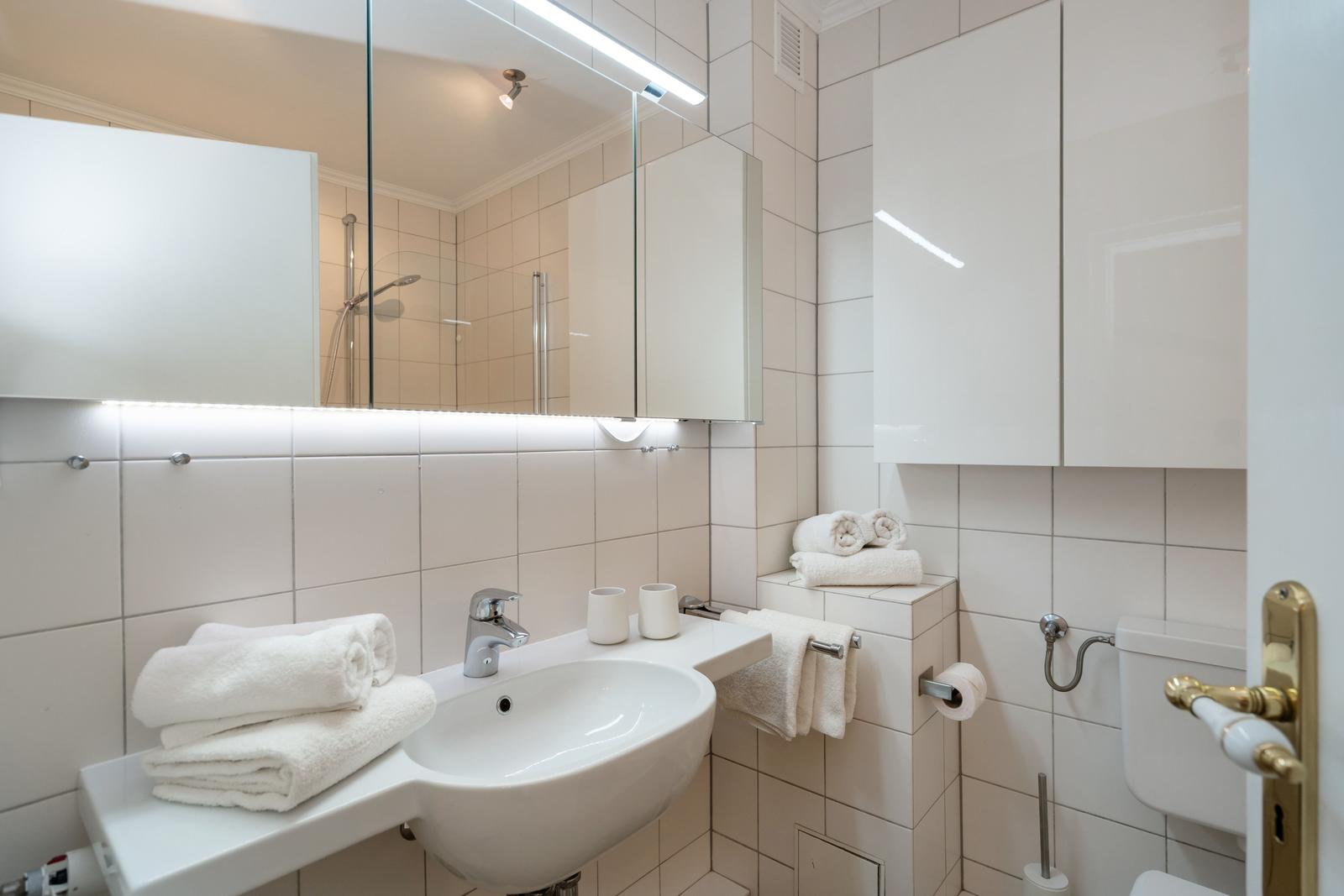 Badezimmer mit Waschbecken, Spiegel, Dusche und Handtüchern.