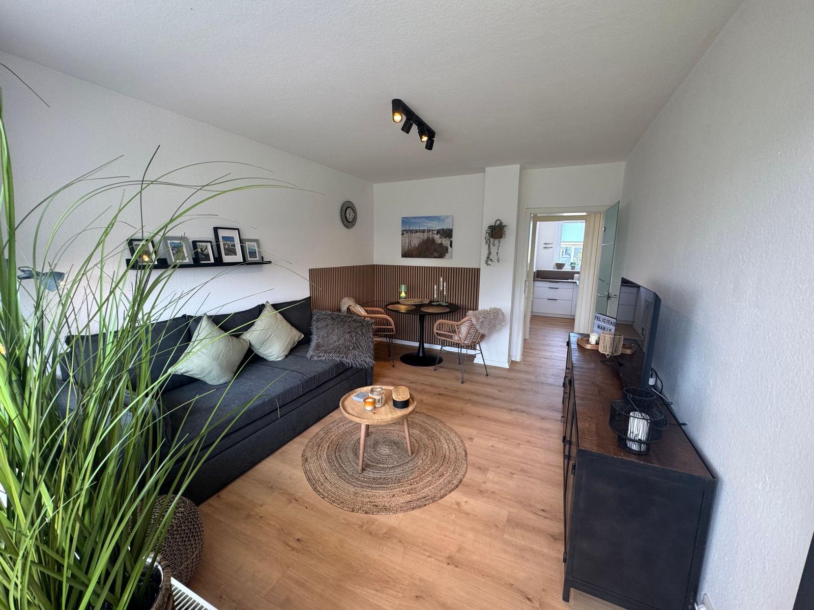 Wohnzimmer mit Sofa, Couchtisch und Essbereich. Holzfußboden und Blick in die Küche.