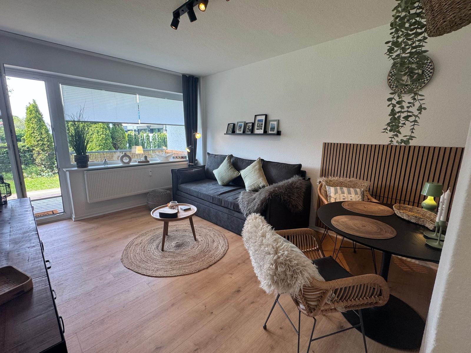 Wohnzimmer mit Sofa, Esstisch und Terrassentür. Holzboden und Pflanzen.