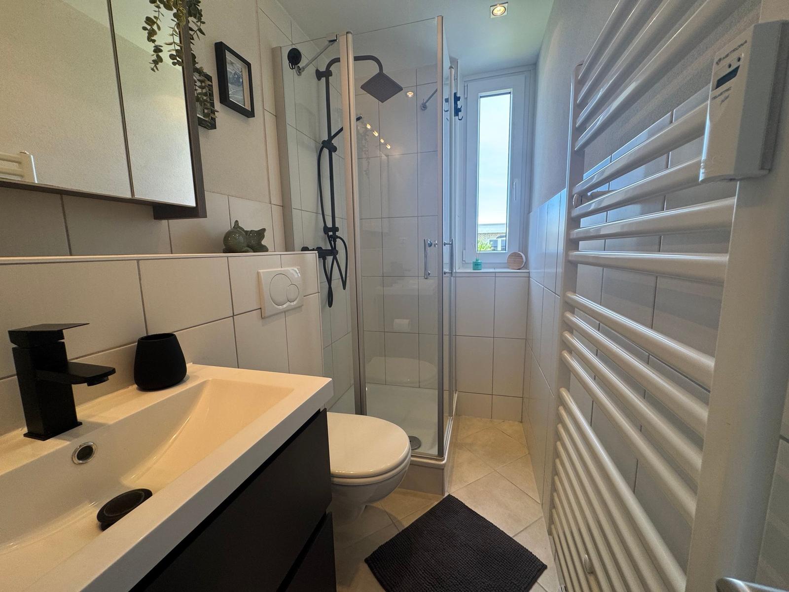 Badezimmer mit Dusche, Waschbecken und Heizung.