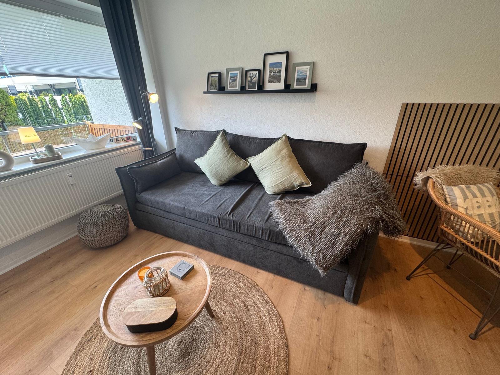 Ein Wohnzimmer mit grauem Sofa, Holzboden und runden Tisch.