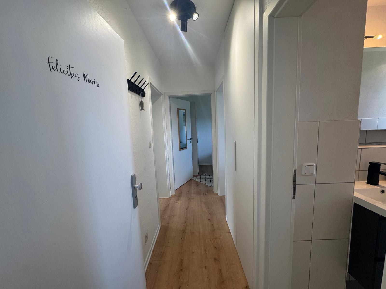 Flur mit Holzboden und Wand mit Schriftzug. Küche und Zimmer sind sichtbar.