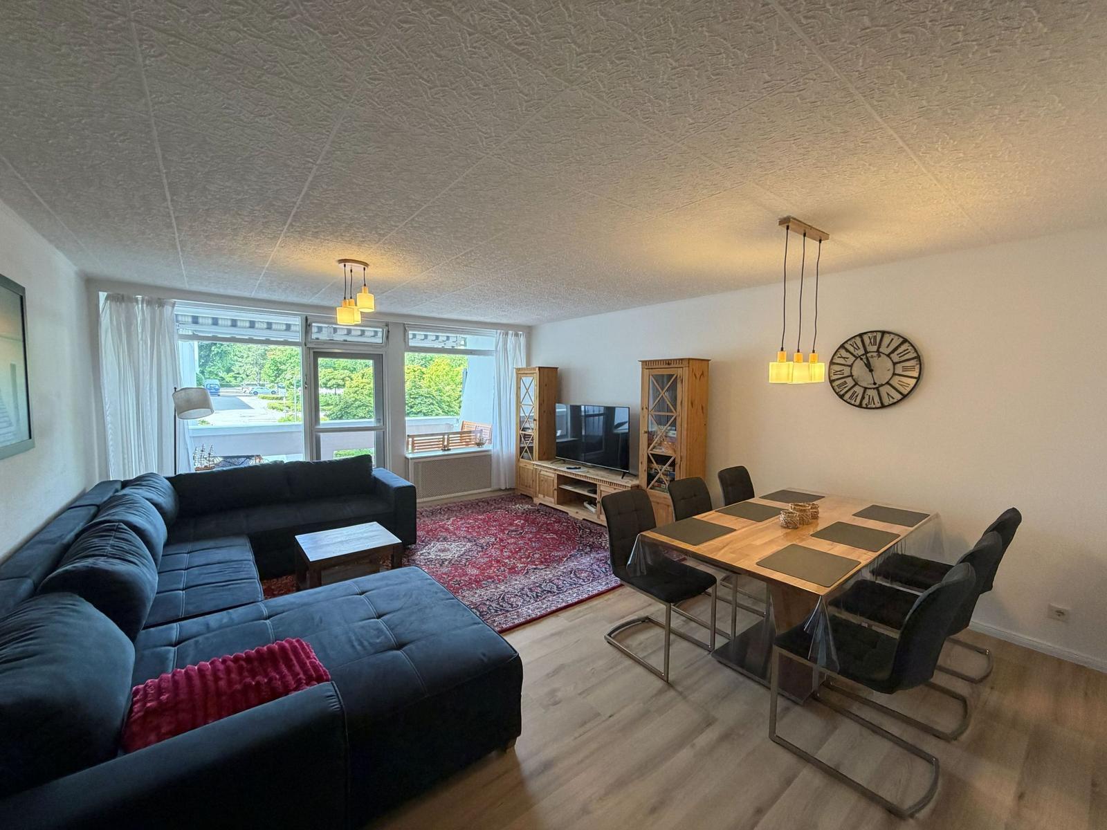 Wohn- und Essbereich mit Sofa, Tisch und Stühlen sowie TV und Wanduhr.