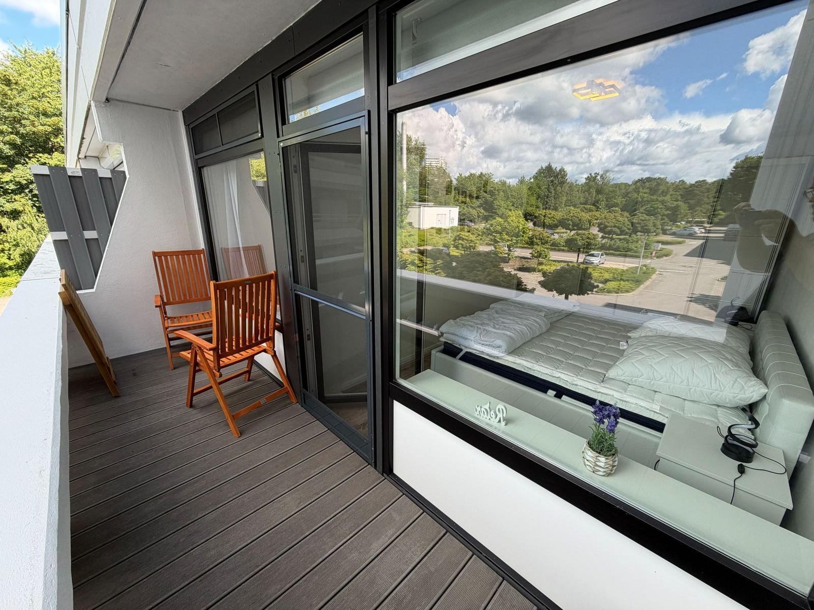 Terrasse mit Holzstühlen und Blick ins Schlafzimmer mit Bett und Fenster.