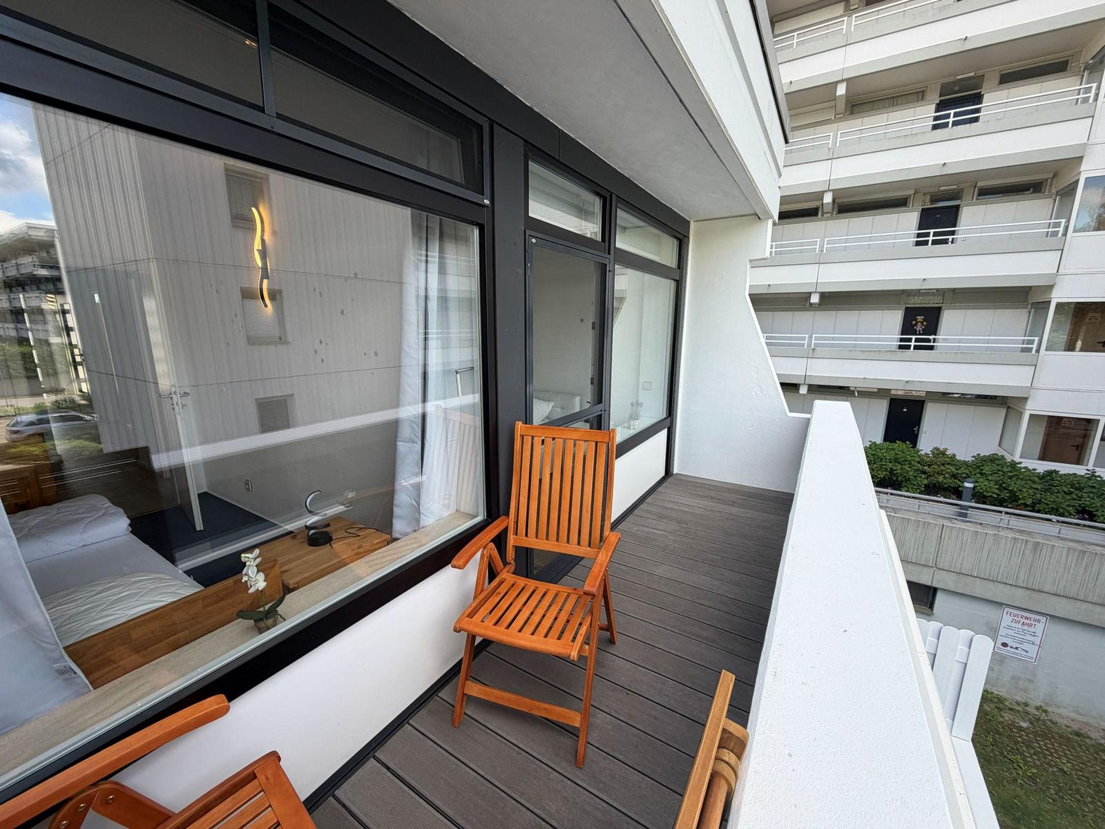 Terrasse mit Holzstuhl und Blick in Wohnraum mit Bett und Fenster