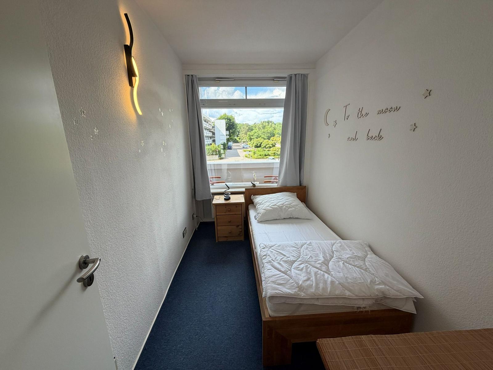 Ein Schlafzimmer mit Bett, Nachttisch und Fenster mit Blick nach draußen.