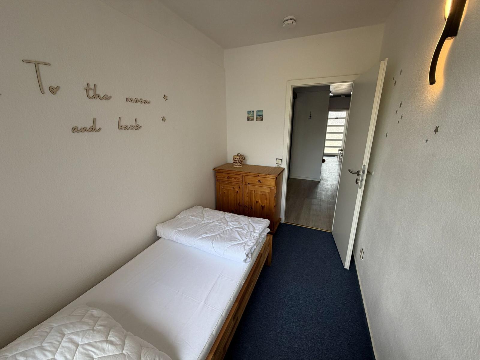 Schlafzimmer mit Bett, Holzkommode und Wanddekoration.