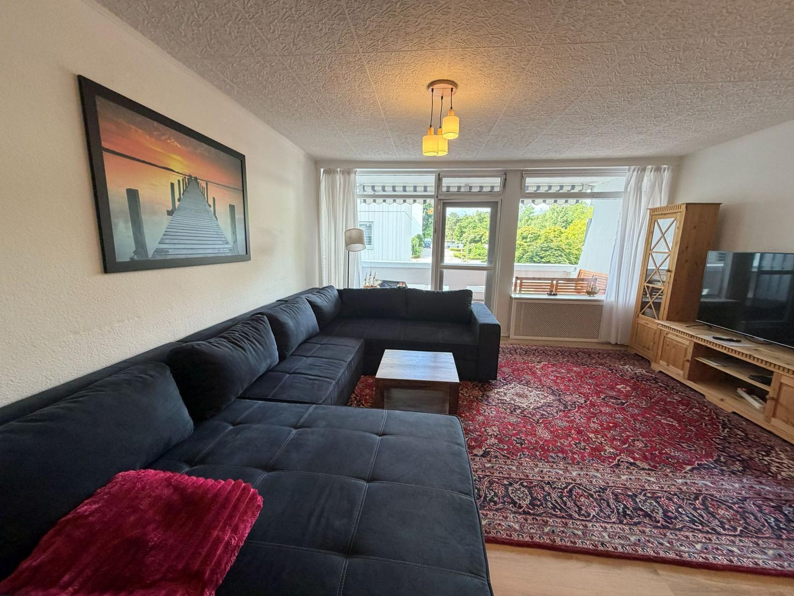 Großer Wohnbereich mit Sofa, Teppich und TV. Blick auf Balkon.