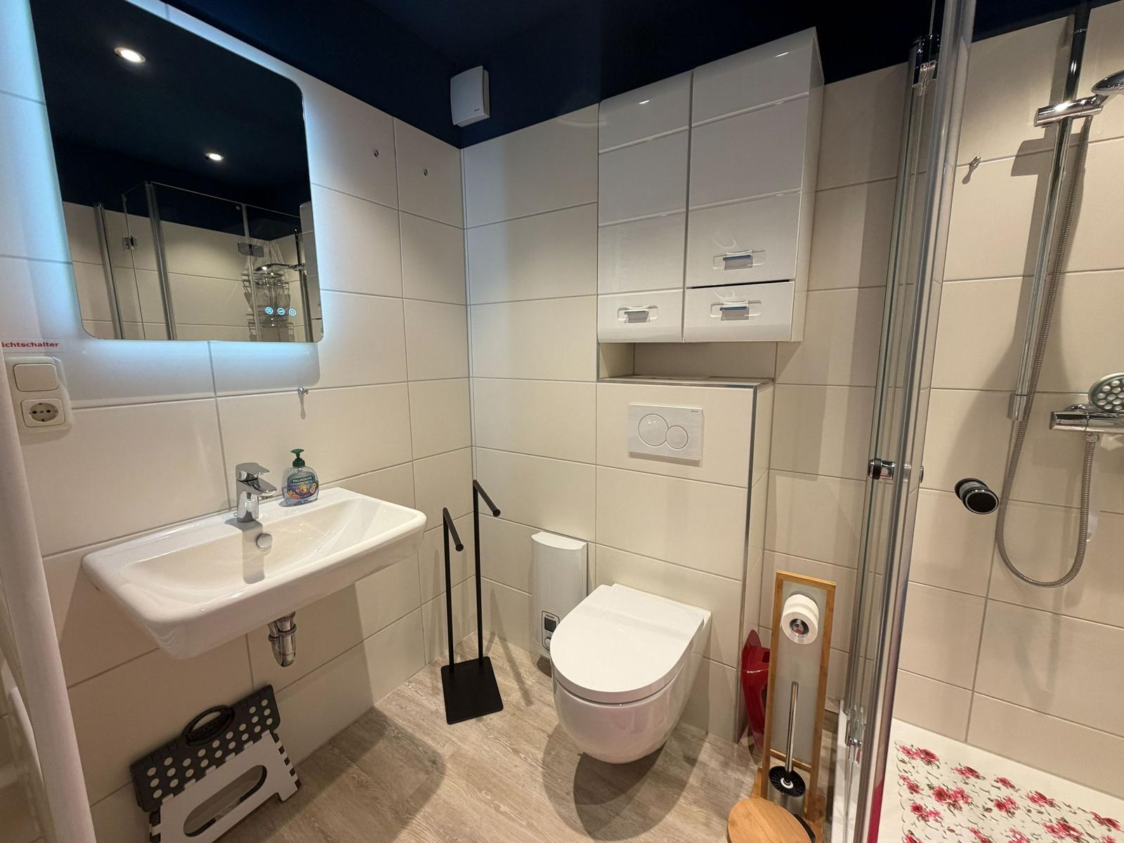 Badezimmer mit Dusche, WC und Waschbecken mit beleuchtetem Spiegel.