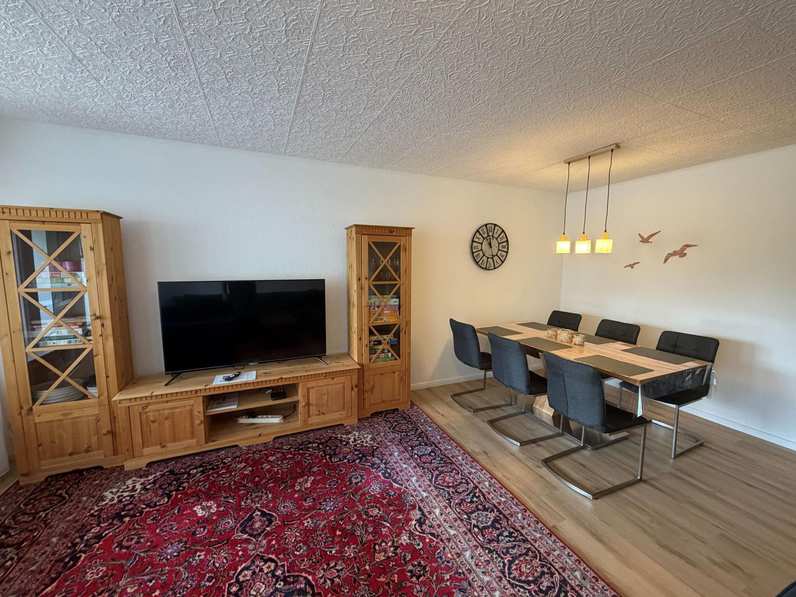 Wohn- und Essbereich mit TV, Esstisch und rotem Teppich.
