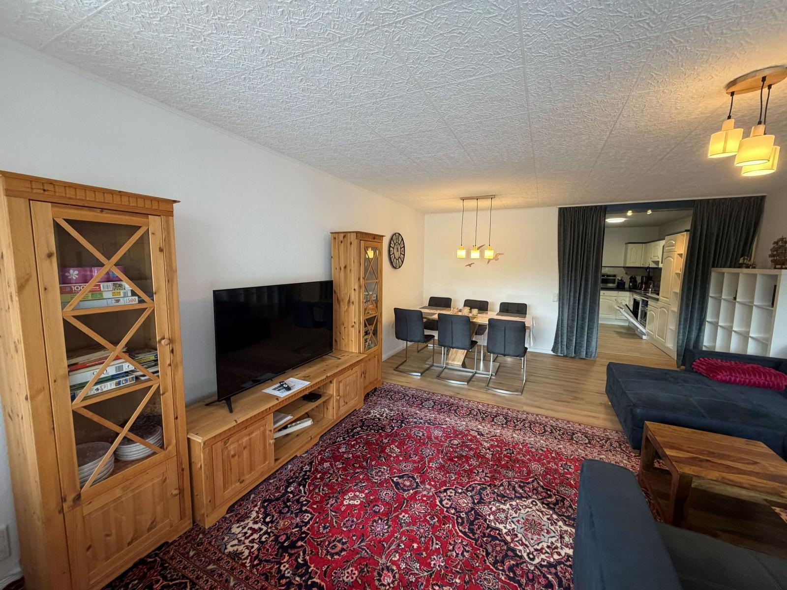 Wohnzimmer mit TV, Esstisch und Küche im Hintergrund.