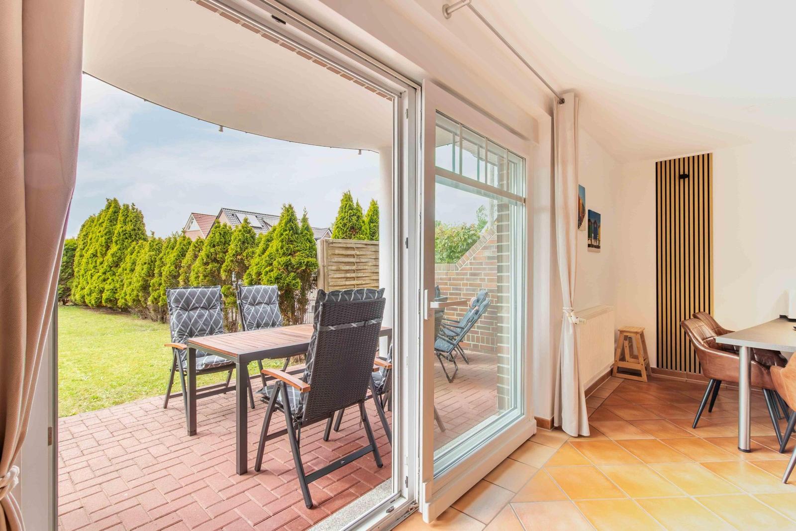 Terrace with table and chairs, view of green garden and fence.