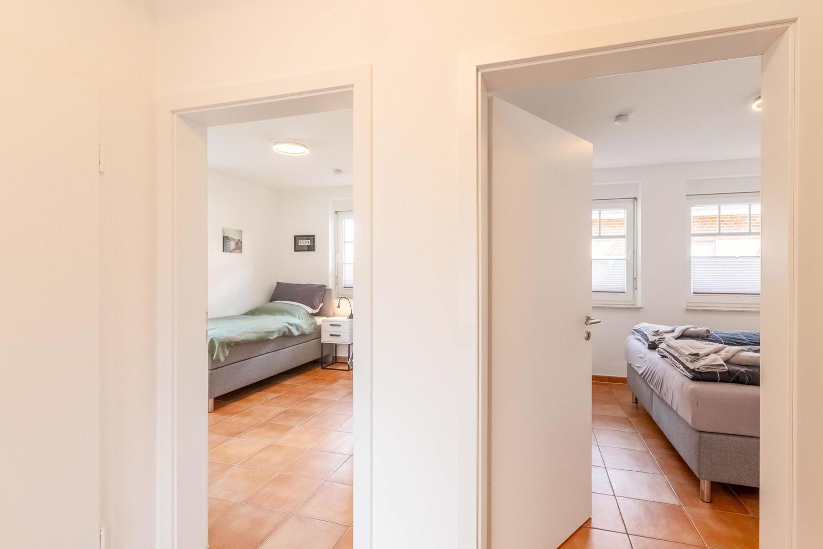 Two bedrooms with beds, windows, and terracotta flooring are visible.