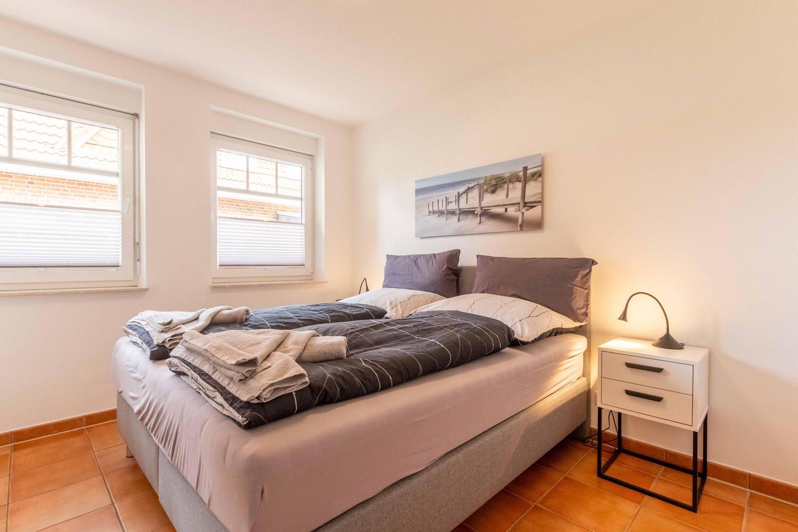 Bedroom with double bed, two windows, and nightstand with lamp.