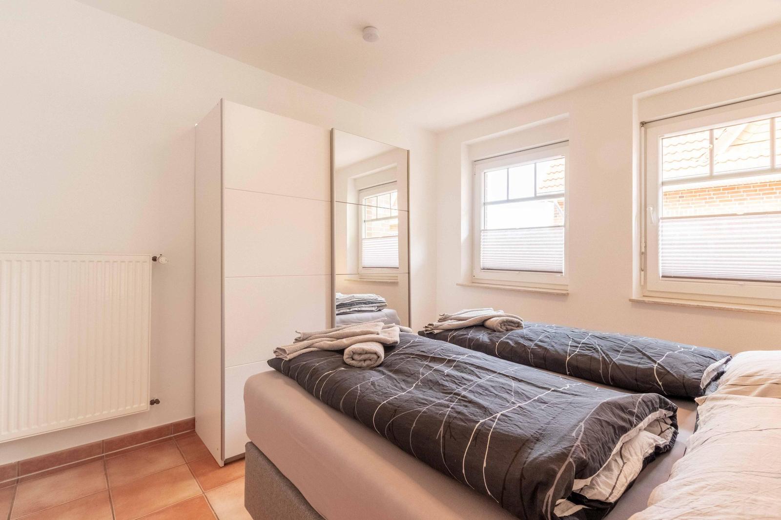 Room with double bed, mirrored wardrobe, and two windows with blinds.
