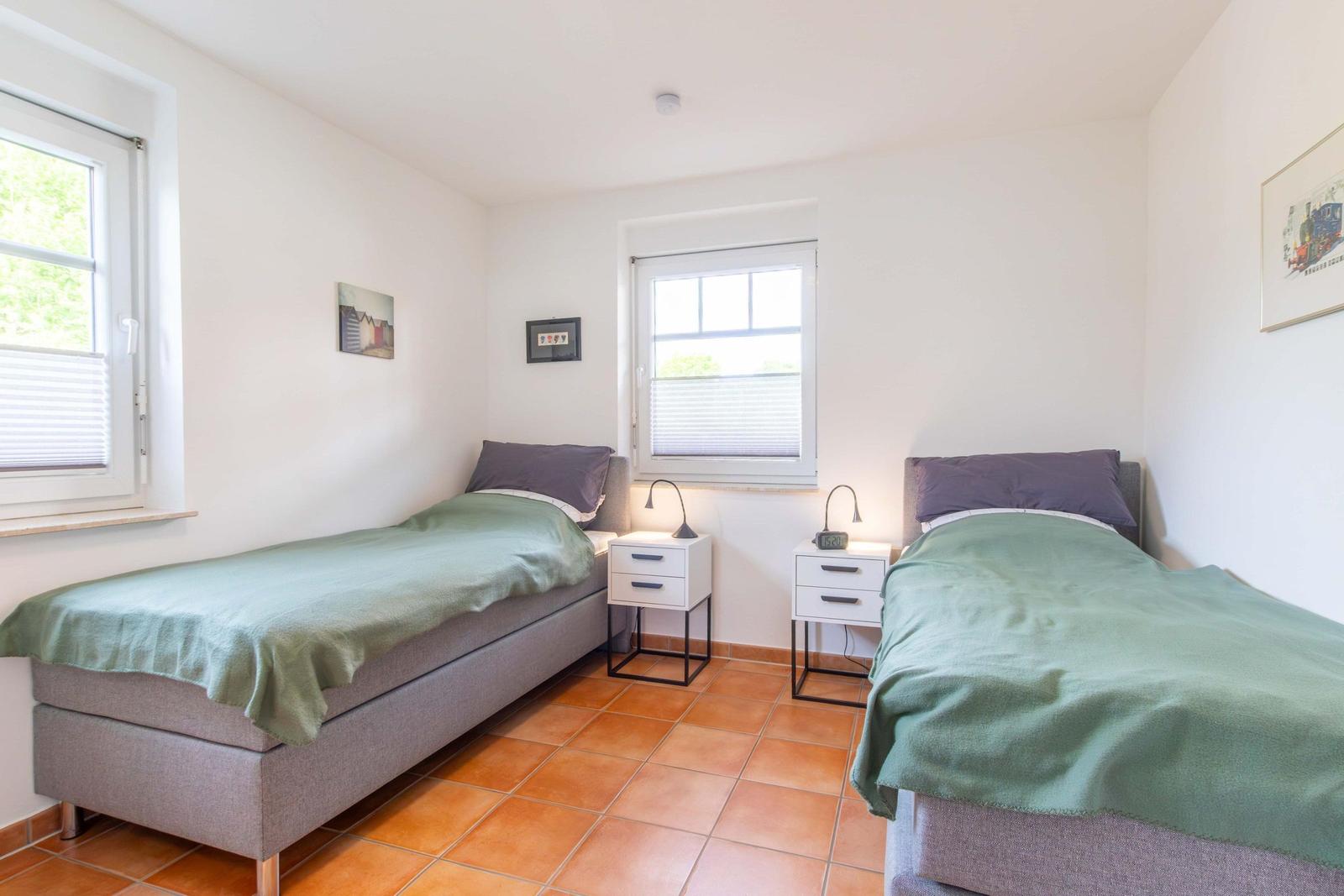 Two single beds with green bedspreads, nightstands, and windows with blinds.