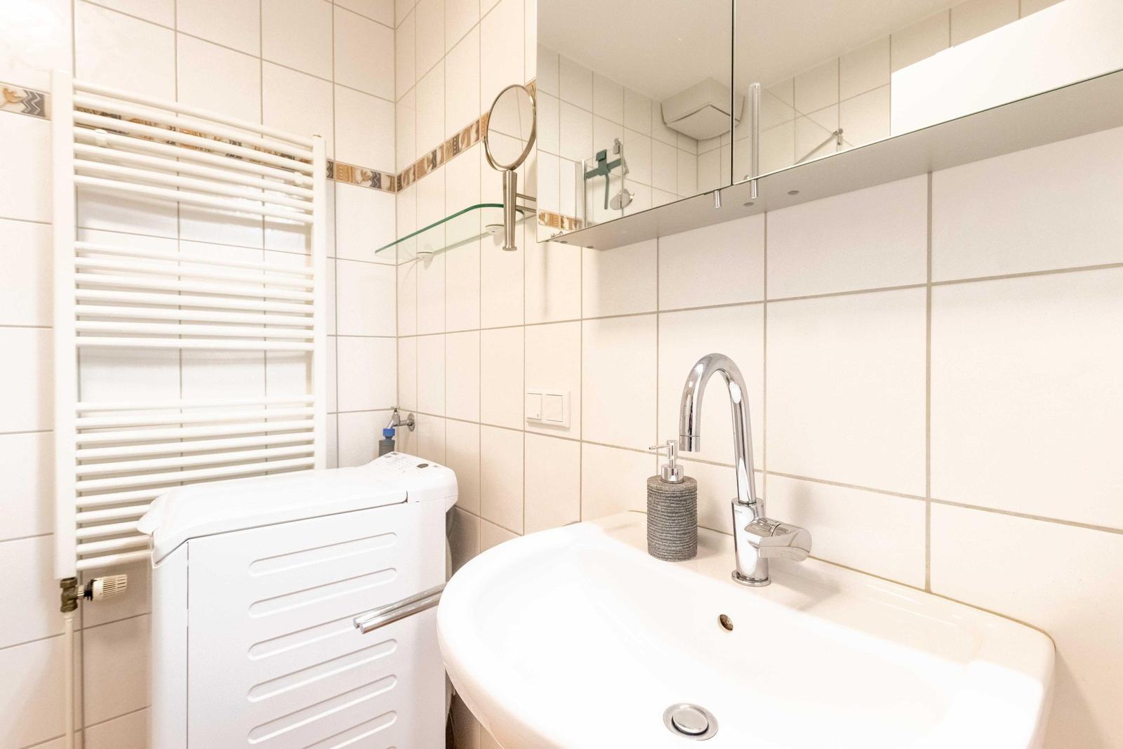 Bathroom with washing machine, mirror, and towel warmer on the wall.