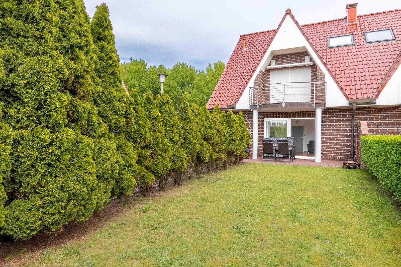 House with red roof, balcony, and garden with table and chairs.