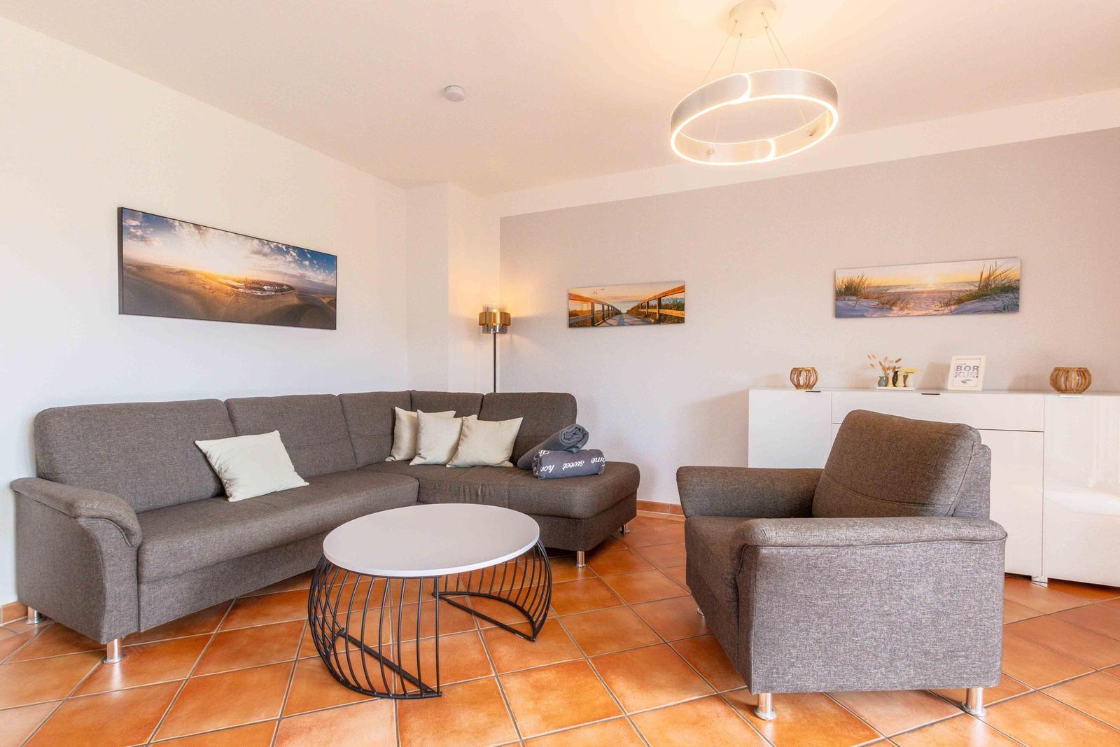 Living room with gray sofa, armchair, and round table on terracotta floor.