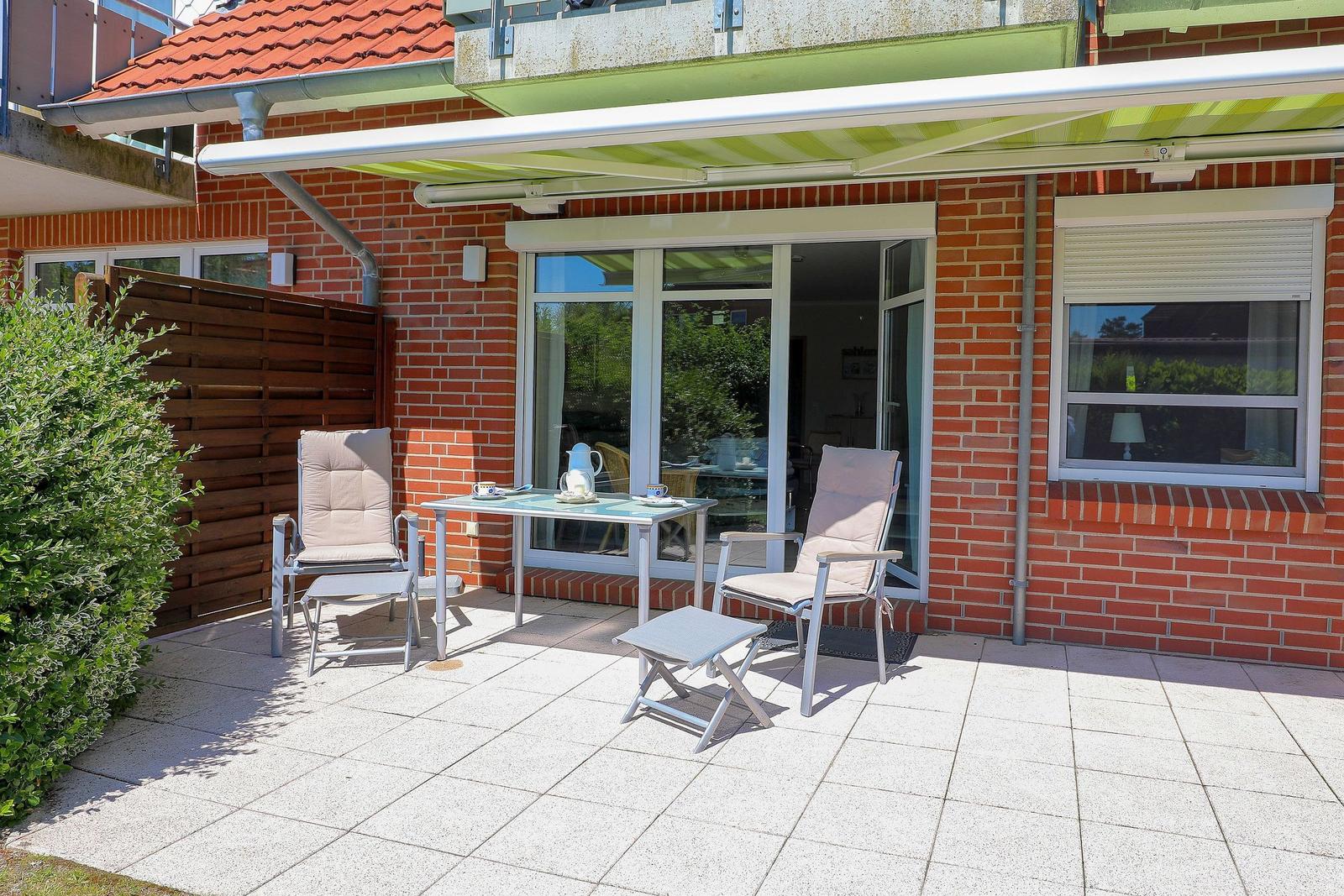 Terrasse mit Tisch, zwei Stühlen und Sonnenschutz vor einem Haus mit Backsteinmauer.