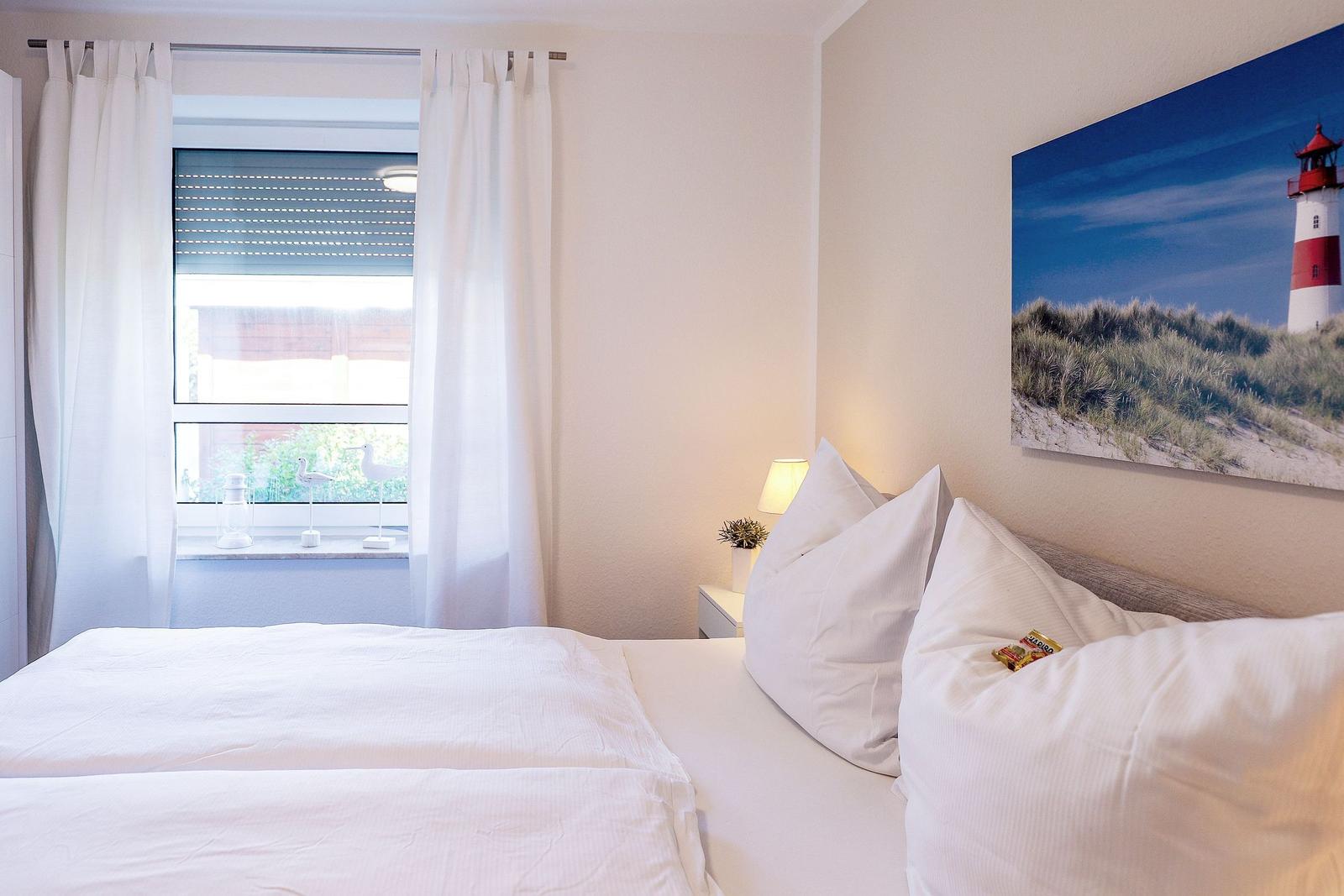 Schlafzimmer mit Bett, Fenster und Wandbild eines Leuchtturms.