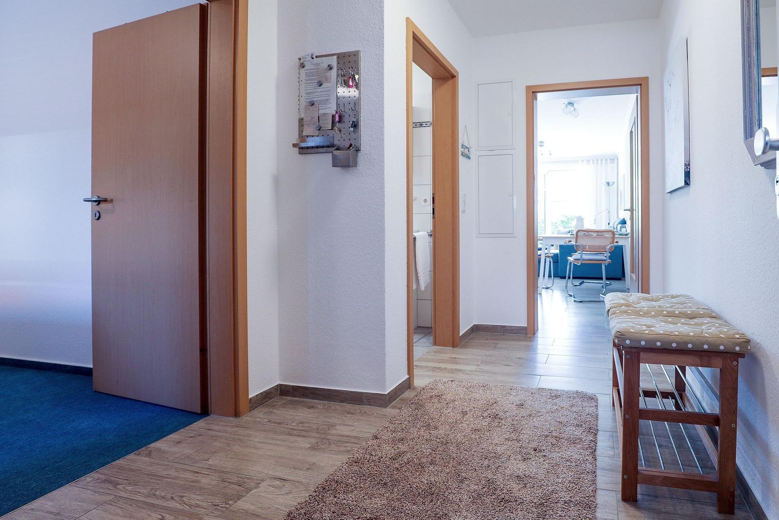 Eingangsbereich mit Holzboden, Teppich und Sitzbank. Tür und Blick in Wohn- und Badezimmer.
