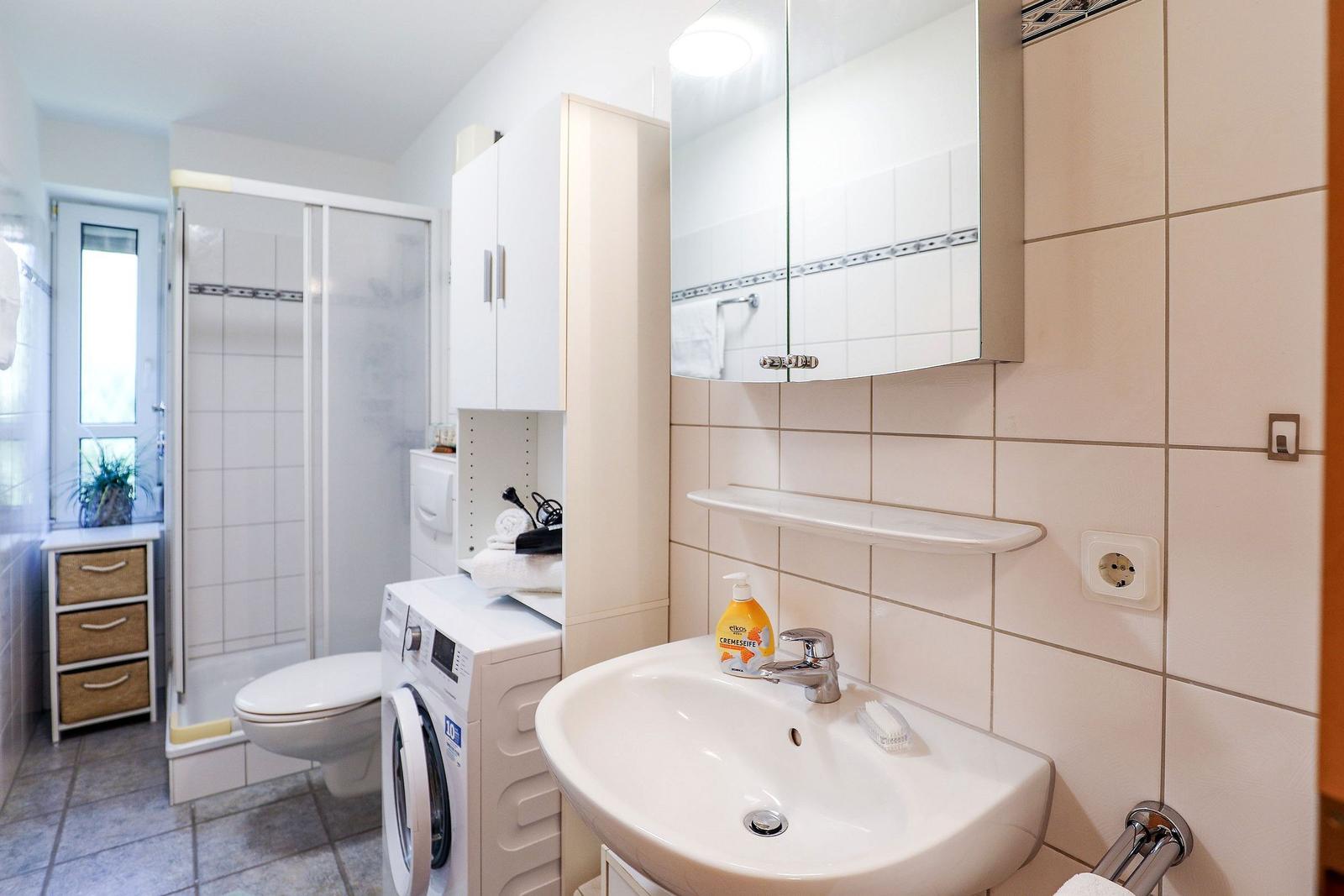 Badezimmer mit Waschmaschine, Dusche und Spiegel