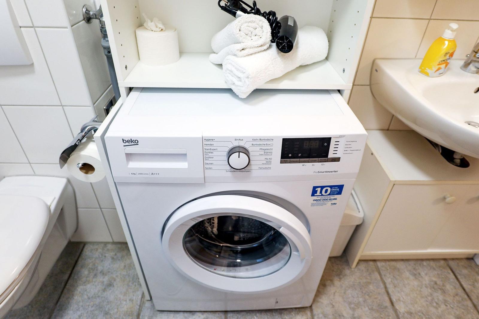 Waschmaschine im Badezimmer mit Handtuch und Haartrockner auf Regal.