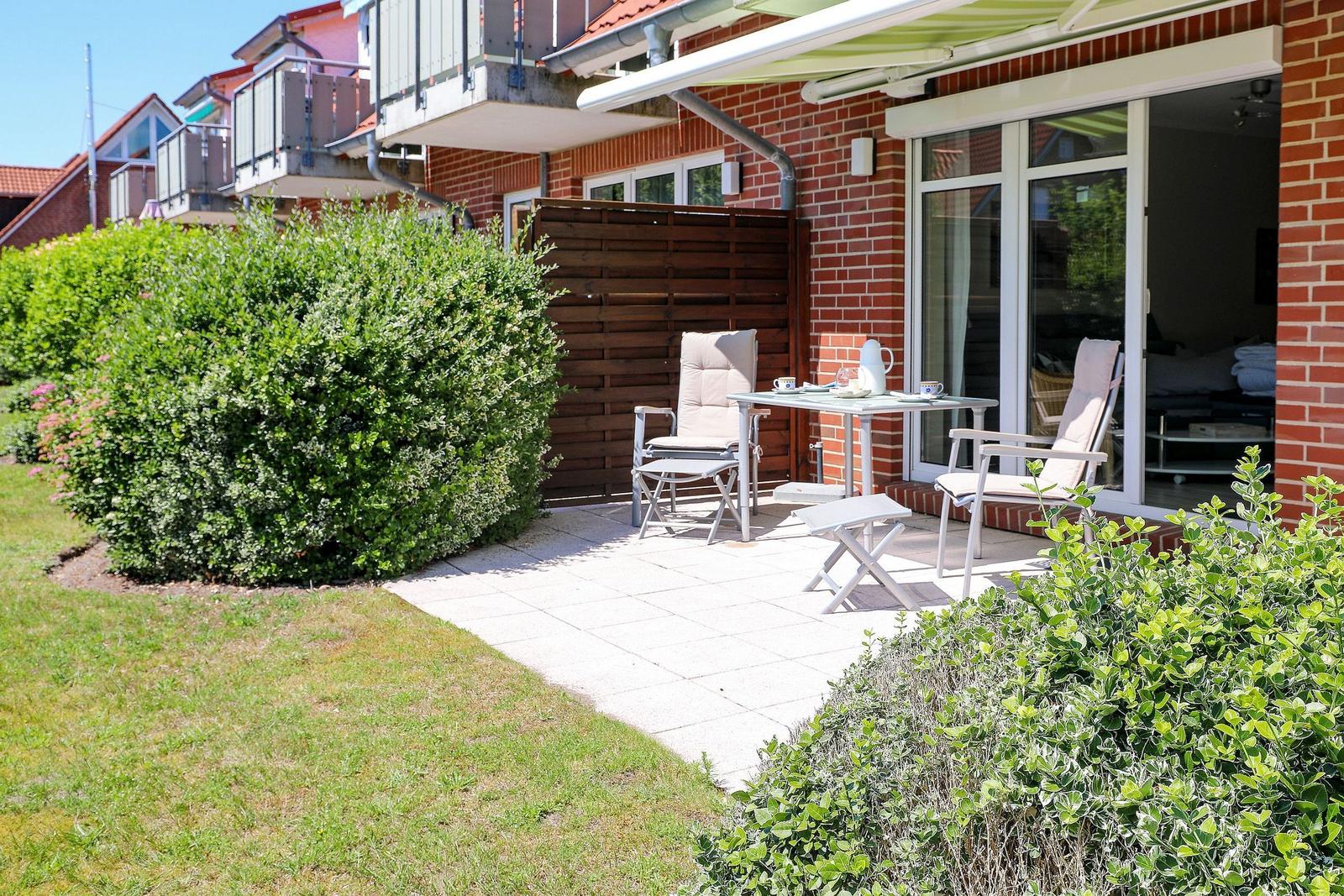 Terrasse mit Tisch und zwei Stühlen, umgeben von Grünflächen und einem Holzzaun.