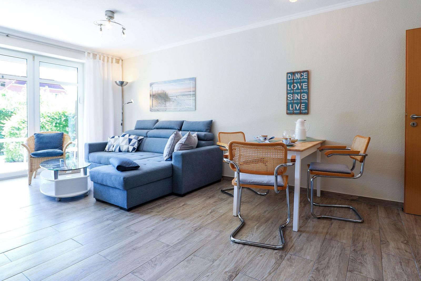 Wohn- und Essbereich mit Sofa, Tisch und Stühlen. Durchgangstür und Fenster sichtbar.