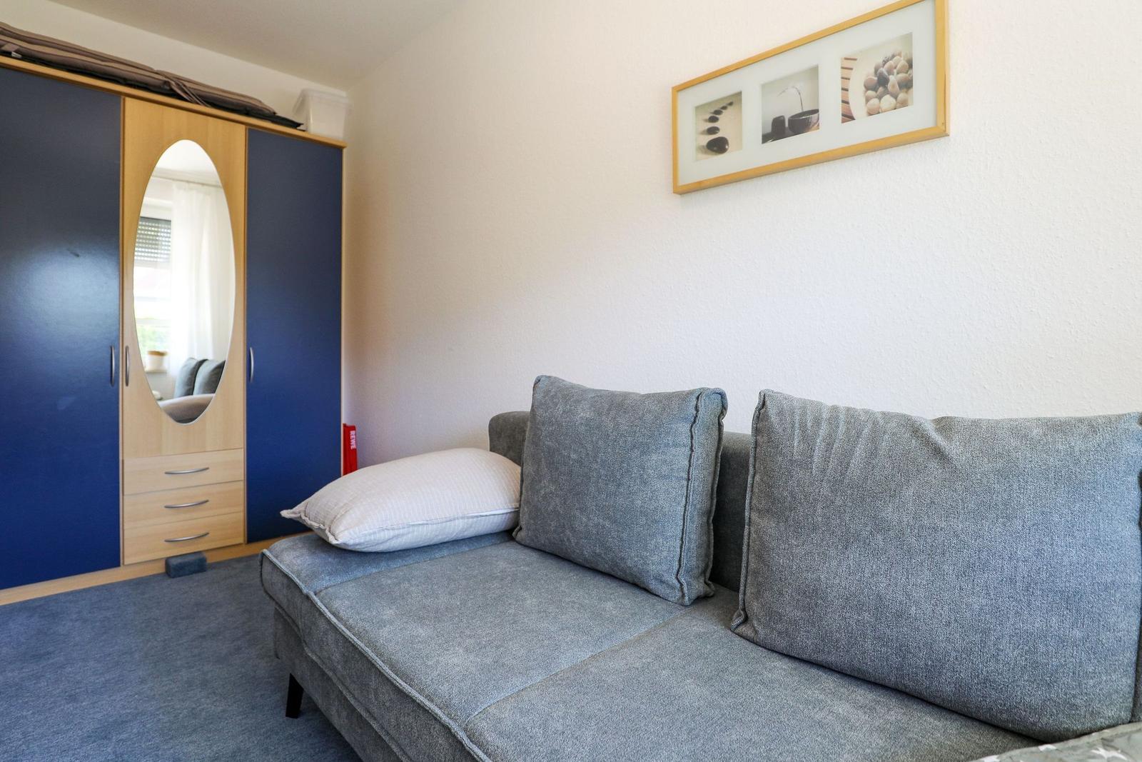 Graße Couch mit Kissen, Kleiderschrank mit Spiegel und Wandbild.