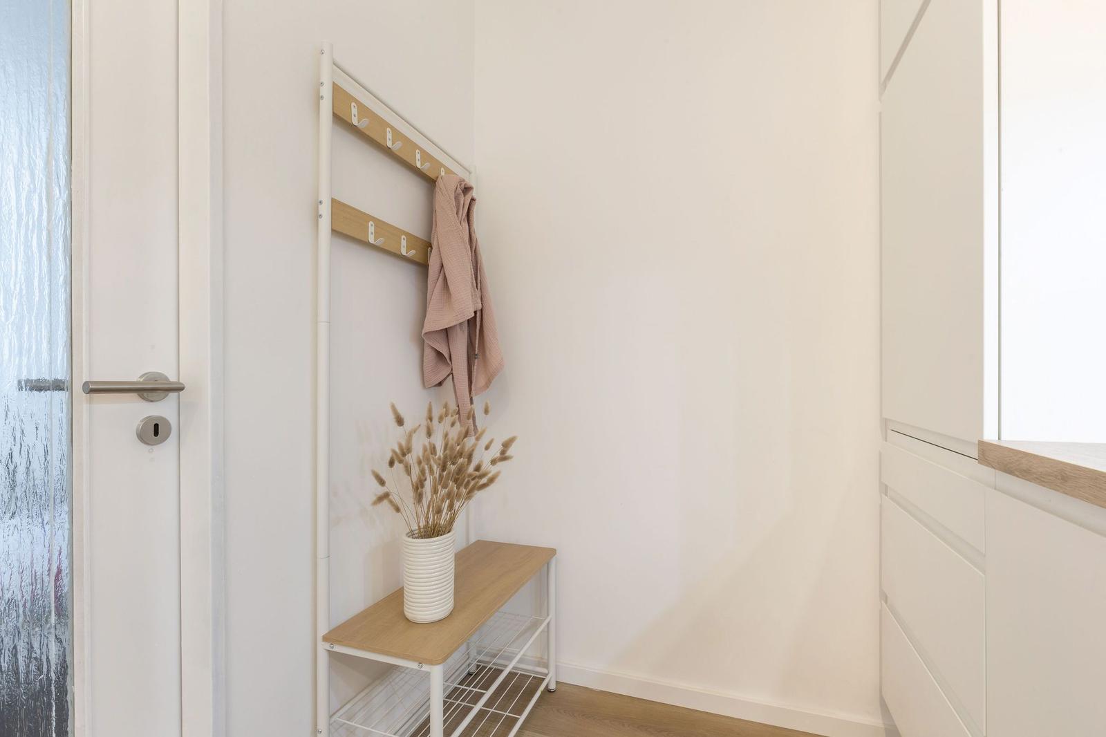 Eingangsbereich mit Kleiderständer, Holzbank und Vase mit Trockenblumen.