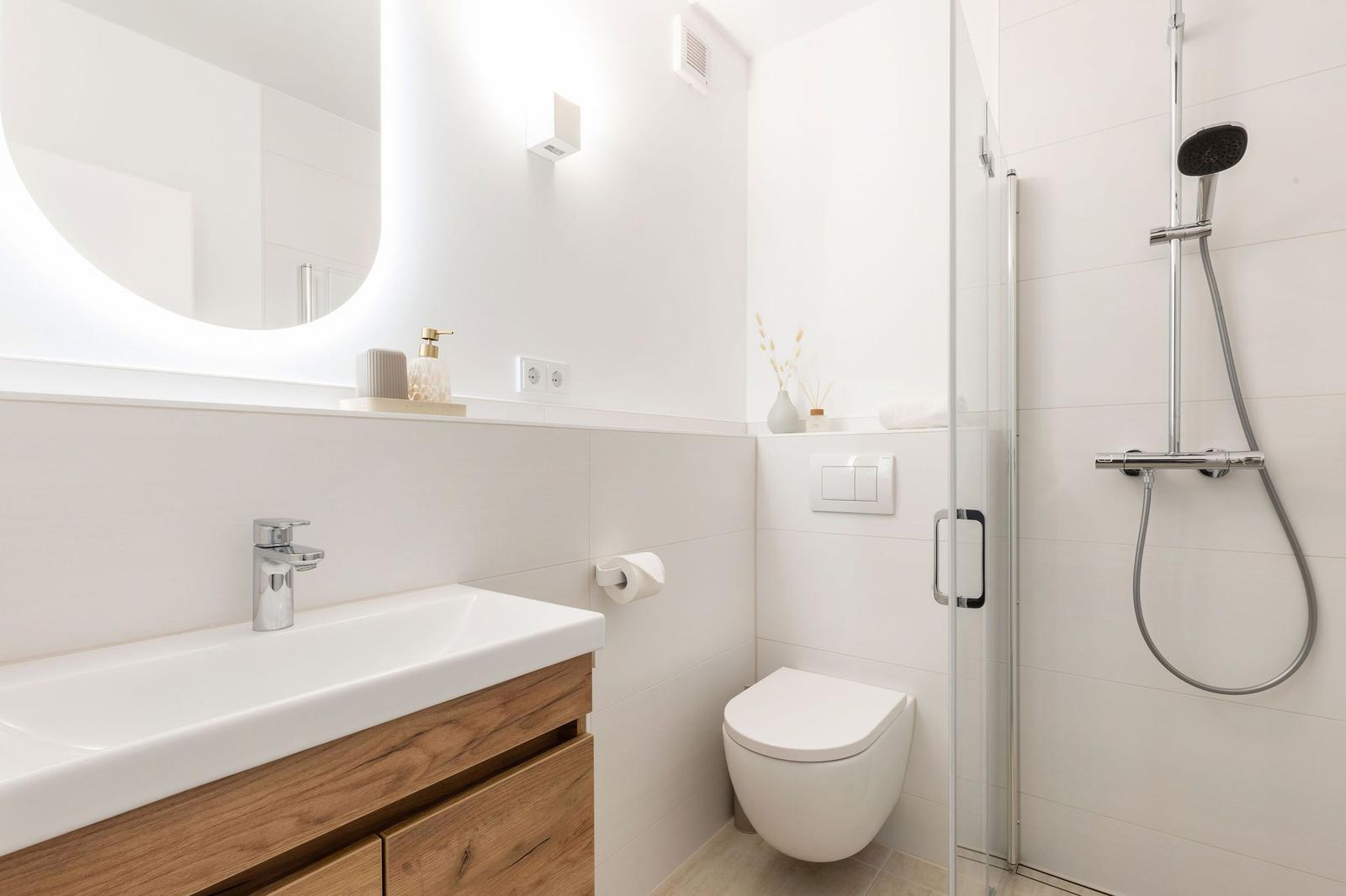 Badezimmer mit Dusche, Toilette und Waschbecken mit Holzunterschrank.