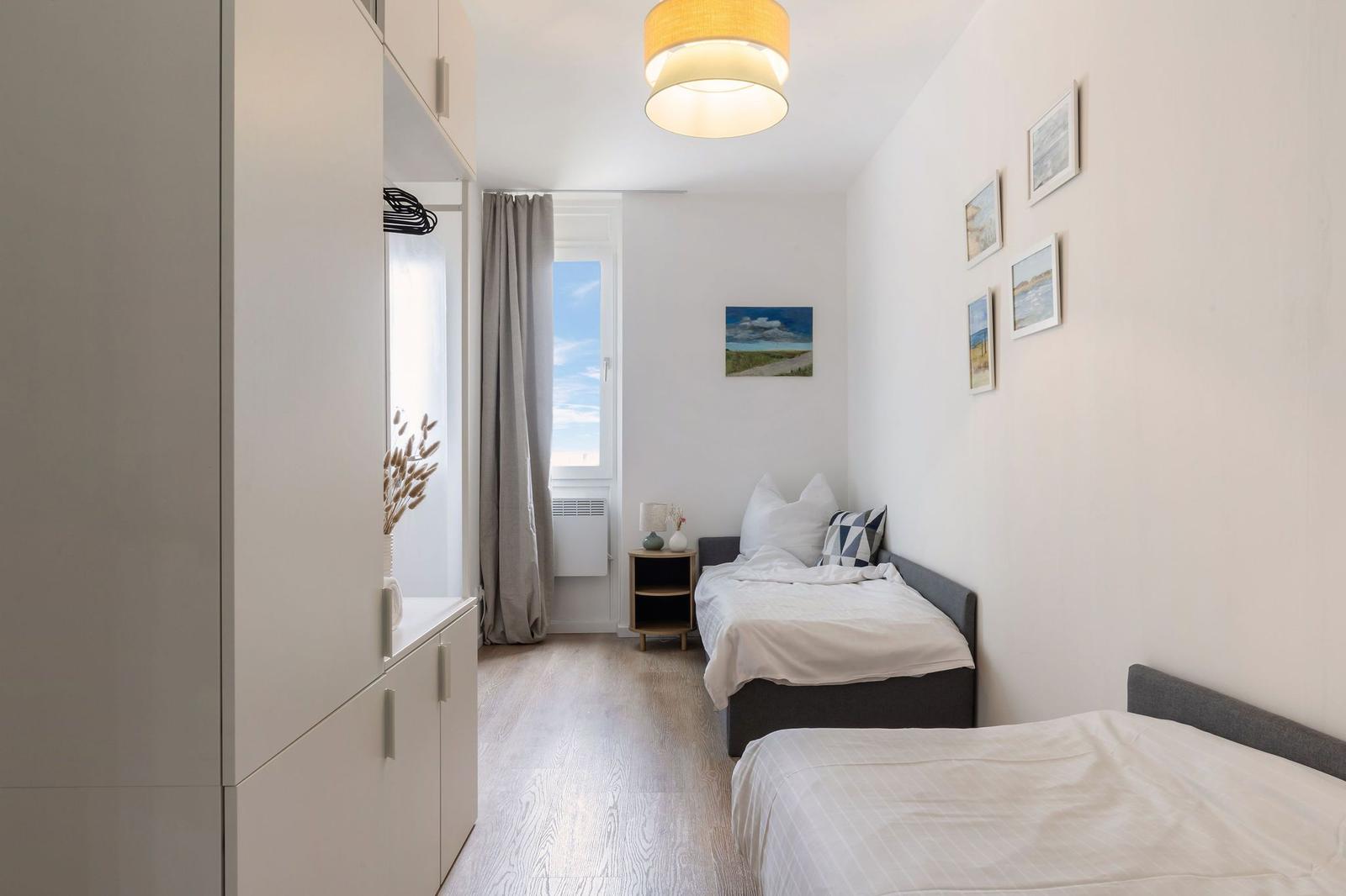 Zwei Betten, Kleiderschrank, Fenster und Wandbilder im Schlafzimmer.