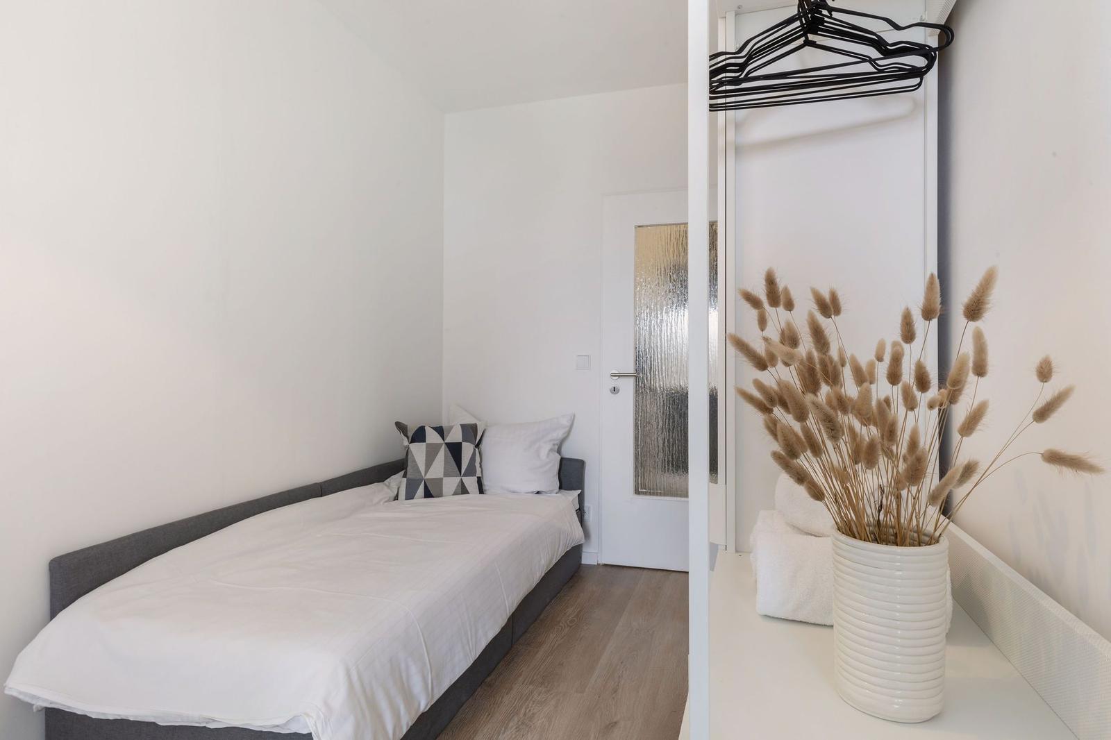 Ein Schlafzimmer mit Bett, Kleiderschrank und Vasen mit Trockenblumen.