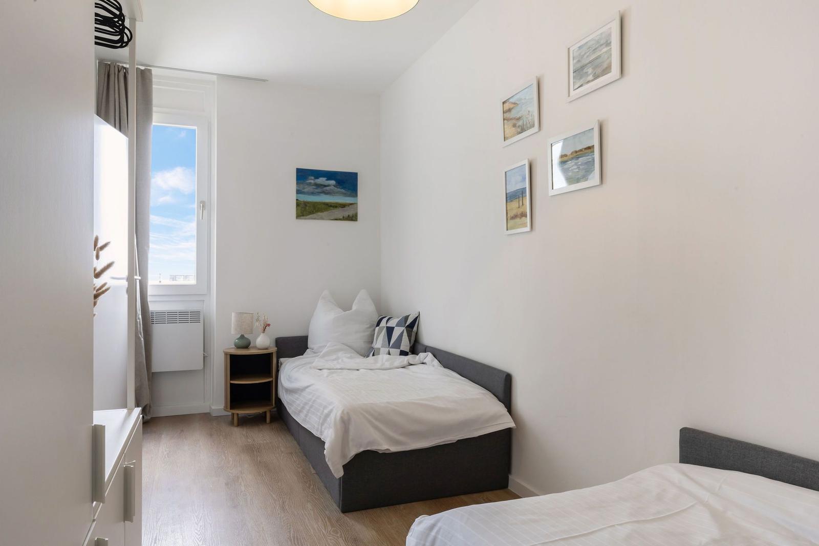 Schlafzimmer mit zwei Betten, Fenster und Wandbildern.